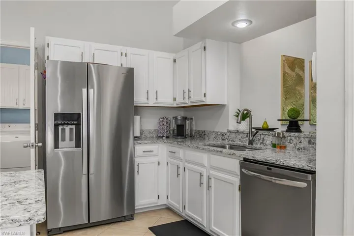 Kitchen featuring stainless steel appliances, a sink, washer / clothes dryer, light tile patterned floors, and white cabinets