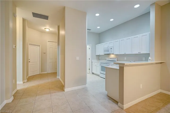 Kitchen with white appliances, white cabinets, light tile flooring, and kitchen peninsula