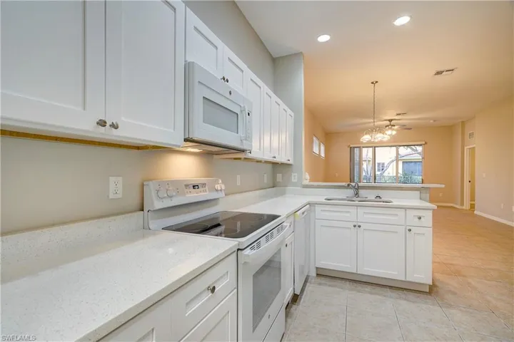 Kitchen featuring white appliances, white cabinets, kitchen peninsula, sink, and light tile flooring