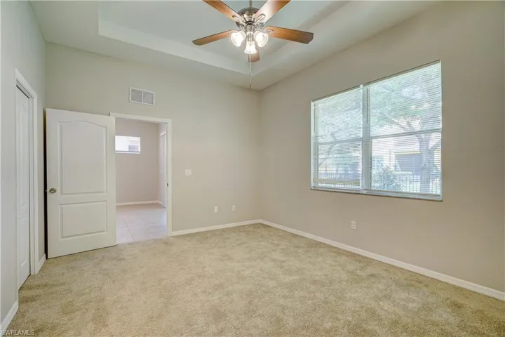 Spare room featuring a raised ceiling, ceiling fan, and light carpet