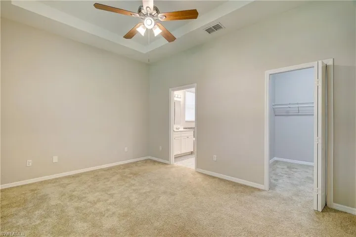 Unfurnished bedroom featuring light carpet, a walk in closet, a closet, and ceiling fan