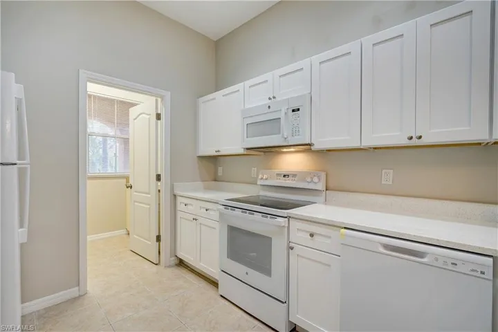 Kitchen featuring white cabinetry, white appliances, light tile flooring, and light stone countertops