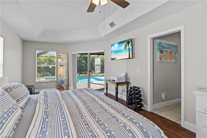 Bedroom featuring a raised ceiling, dark wood-style floors, ceiling fan, and access to outside