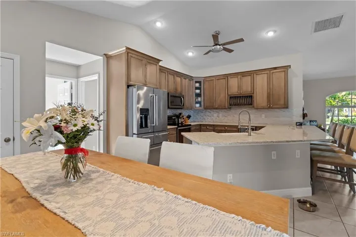 Kitchen featuring a peninsula, appliances with stainless steel finishes, light stone countertops, glass insert cabinets, and a breakfast bar