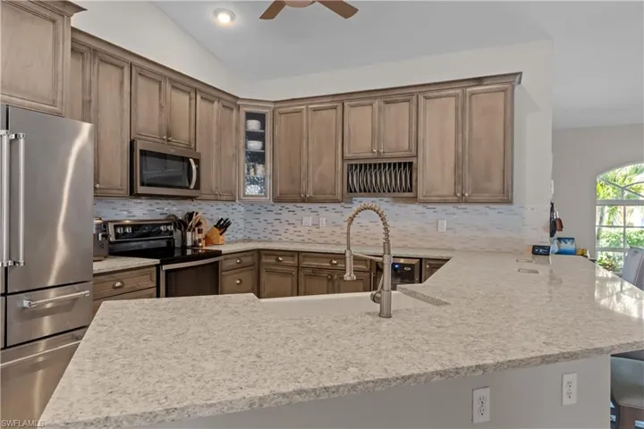 Kitchen with stainless steel appliances, a peninsula, light stone countertops, and vaulted ceiling