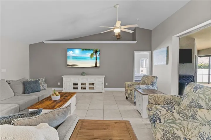 Living room with lofted ceiling, light tile patterned floors, and ceiling fan