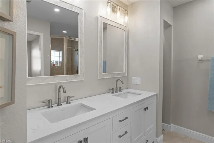 Bathroom with double vanity, a textured wall, and a stall shower