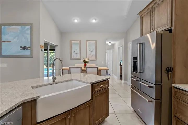 Kitchen with high quality fridge, light stone countertops, light tile patterned floors, and brown cabinets