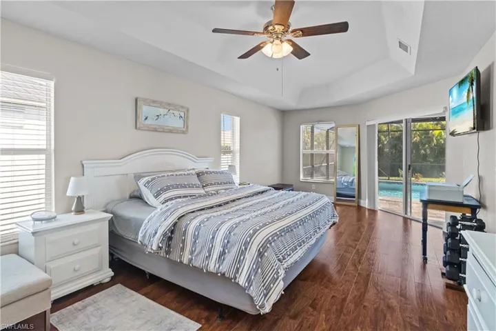 Bedroom featuring dark wood finished floors, a tray ceiling, a ceiling fan, and access to exterior