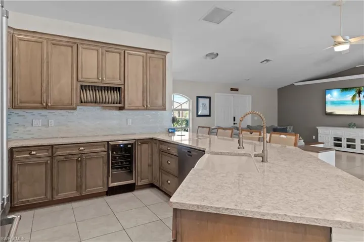Kitchen featuring light tile patterned floors, beverage cooler, light stone countertops, a peninsula, and dishwasher