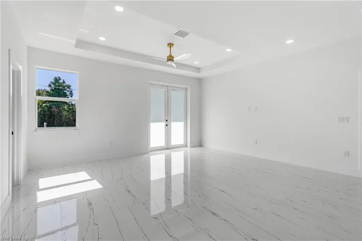 Unfurnished room with french doors, a tray ceiling, light marble finish flooring, recessed lighting, and a ceiling fan