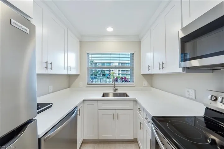 Kitchen with appliances with stainless steel finishes, crown molding, white cabinets, and sink
