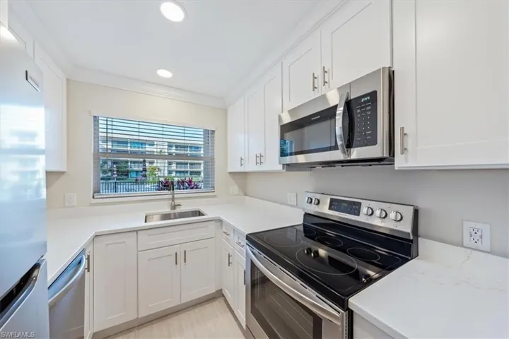 Kitchen with appliances with stainless steel finishes, white cabinetry, sink, and ornamental molding