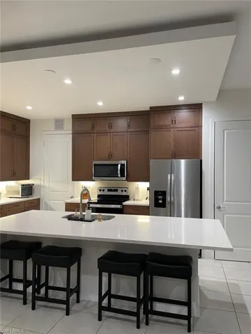 Kitchen with a kitchen bar, stainless steel appliances, light tile patterned floors, dark wood finish cabinetry, and recessed lighting