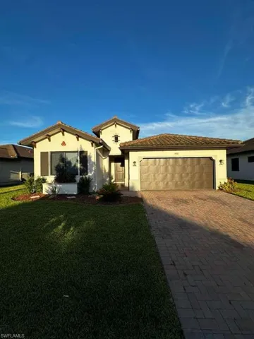 View of front facade featuring stucco siding, decorative driveway, a front yard, and an attached garage