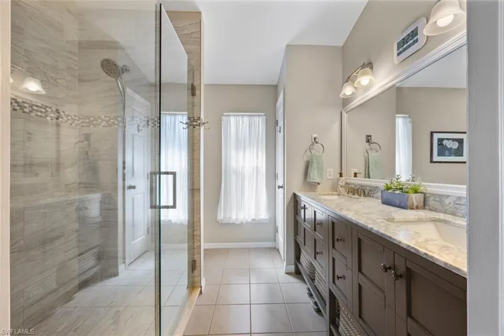 Newly remodeled primary bathroom with dual vanities, walk-in shower, & linen closet.