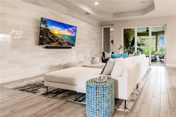 Living area featuring a raised ceiling, wood finished floors, a ceiling fan, and recessed lighting