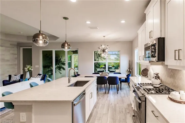 Kitchen with white cabinetry, decorative light fixtures, appliances with stainless steel finishes, recessed lighting, and a center island with sink