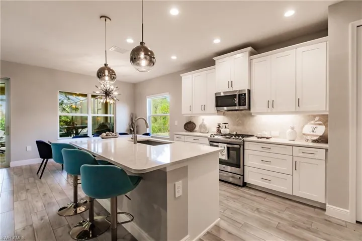 Kitchen with stainless steel appliances, backsplash, pendant lighting, an island with sink, and white cabinets