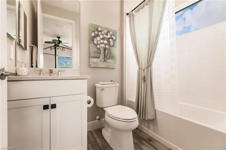 Bathroom featuring shower / bath combination with curtain, vanity, dark wood-type flooring, and ceiling fan