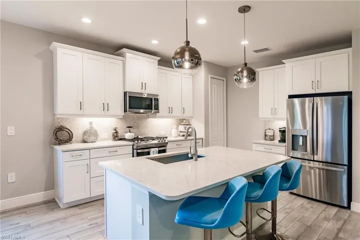 Kitchen featuring appliances with stainless steel finishes, tasteful backsplash, a breakfast bar, a kitchen island with sink, and recessed lighting