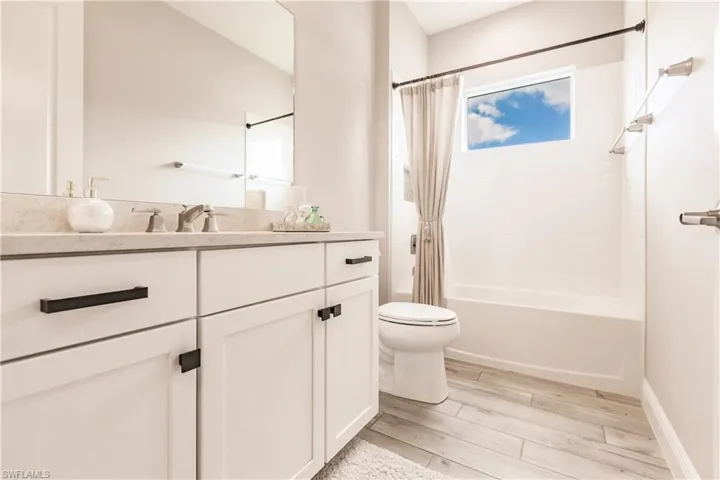 Bathroom with vanity, shower / bathtub combination with curtain, and light wood finished floors