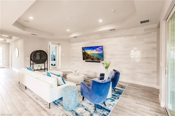Living room with a tray ceiling, light wood-style flooring, recessed lighting, and an accent wall
