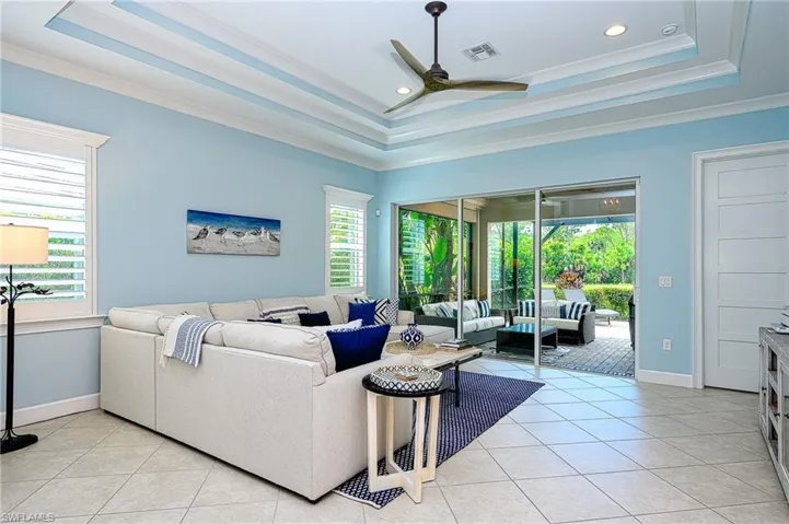 Tiled living room with ceiling fan, ornamental molding, and a tray ceiling