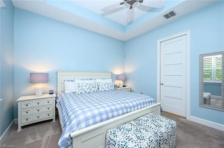 Bedroom featuring ceiling fan, a raised ceiling, and dark colored carpet