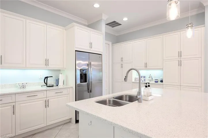 Kitchen featuring white cabinetry, light tile patterned floors, decorative light fixtures, stainless steel fridge with ice dispenser, and crown molding
