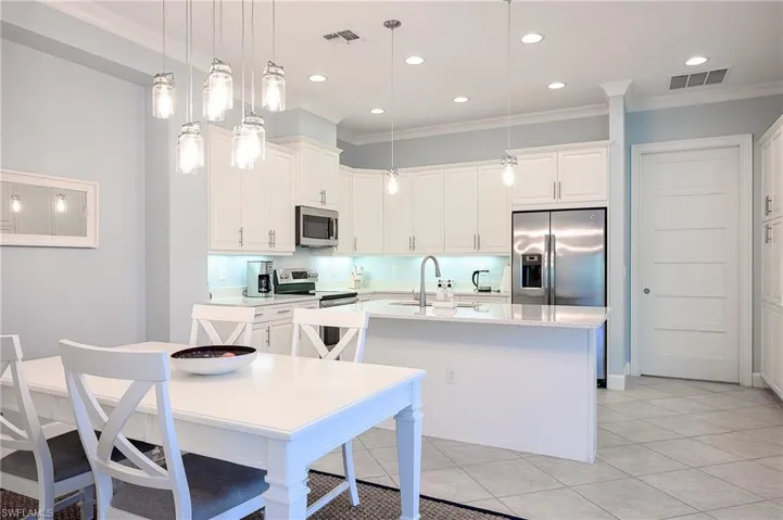 Kitchen with appliances with stainless steel finishes, sink, an island with sink, light stone countertops, and hanging light fixtures