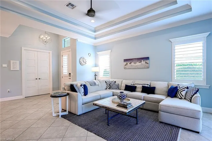 Living room featuring ceiling fan with notable chandelier, a tray ceiling, light tile patterned flooring, and ornamental molding