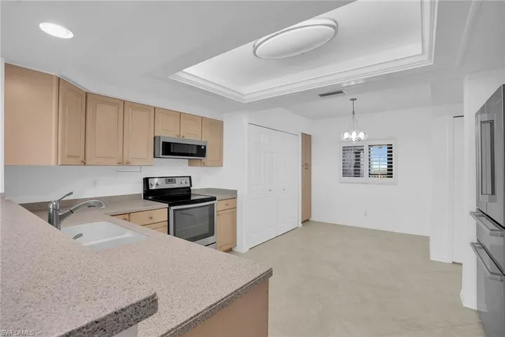 Kitchen featuring stainless steel appliances, light brown cabinets, a tray ceiling, decorative light fixtures, and a chandelier