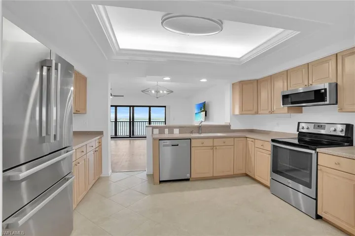 Kitchen with appliances with stainless steel finishes, light brown cabinetry, crown molding, a tray ceiling, and a peninsula