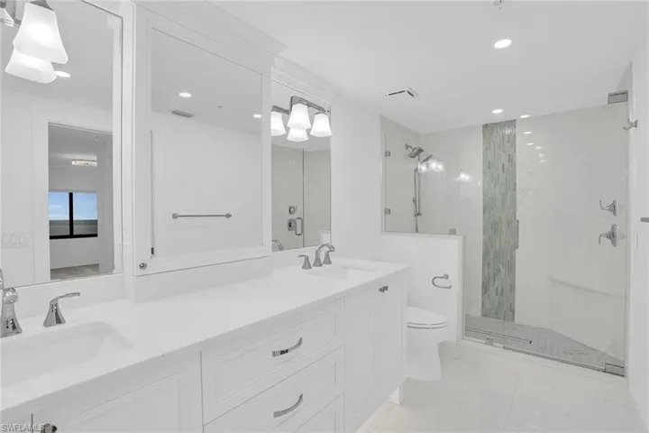 Bathroom featuring double vanity, a marble finish shower, recessed lighting, and light marble finish flooring