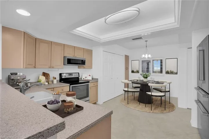 Kitchen with appliances with stainless steel finishes, light brown cabinetry, decorative light fixtures, and a raised ceiling **PHOTO IS VIRTUALLY STAGED**