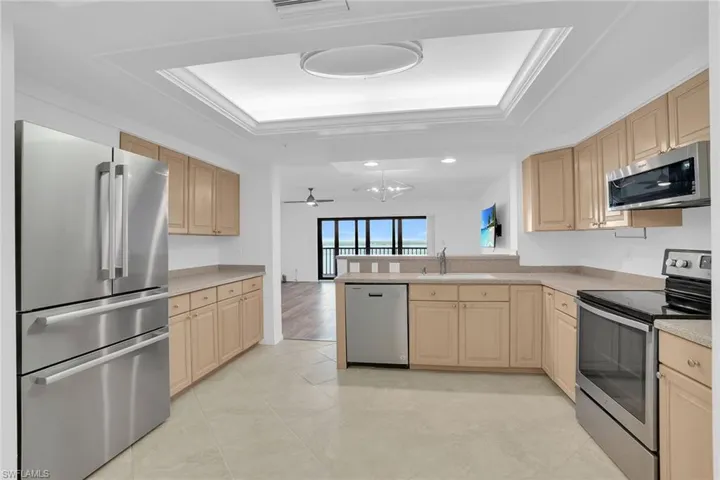 Kitchen with stainless steel appliances, light brown cabinetry, a raised ceiling, a peninsula, and ceiling fan