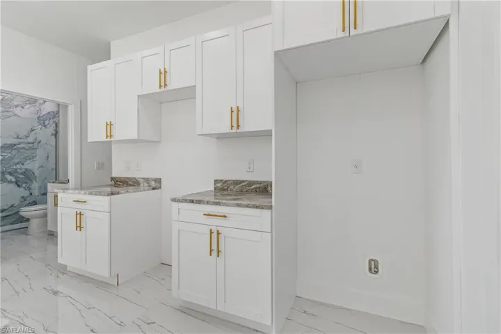 Kitchen with white cabinets, light marble finish floors, and light stone countertops