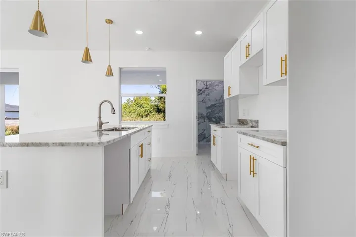 Kitchen featuring white cabinetry, an island with sink, light stone counters, and hanging light fixtures