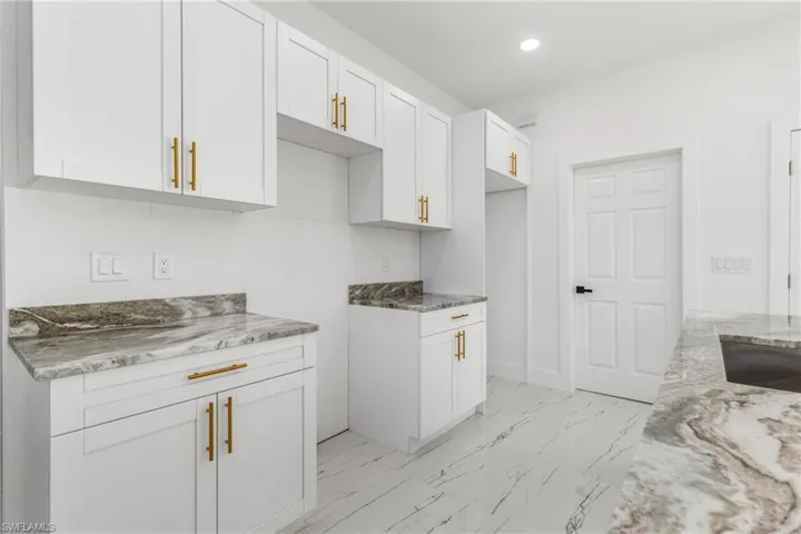 Kitchen with white cabinets, light stone counters, light marble finish floors, and recessed lighting