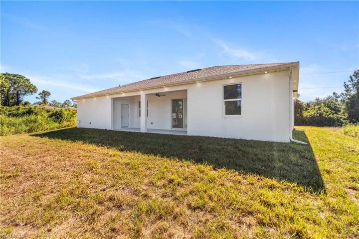 Rear view of house featuring a patio area, a lawn, stucco siding, and a ceiling fan