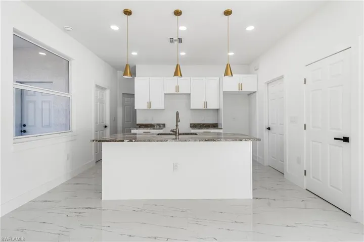 Kitchen with white cabinets, dark stone counters, pendant lighting, a center island with sink, and light marble finish flooring