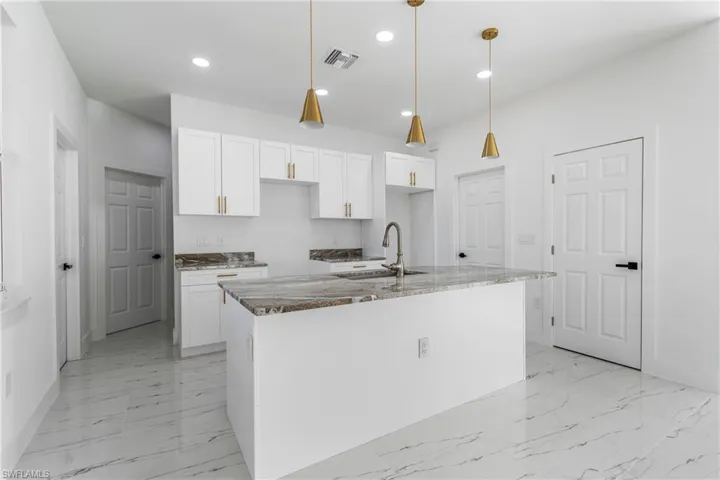 Kitchen featuring white cabinetry, dark stone countertops, pendant lighting, a kitchen island with sink, and light marble finish flooring