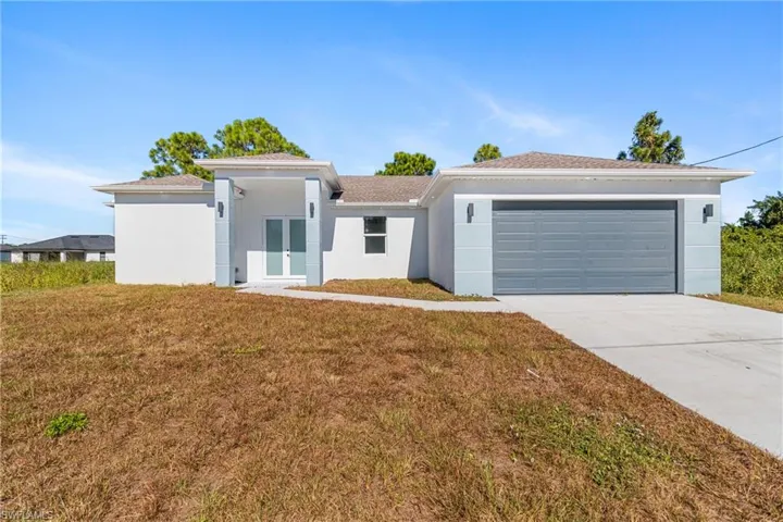 View of front of house with a front yard, french doors, stucco siding, and driveway