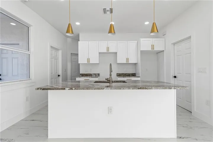 Kitchen featuring white cabinetry, a center island with sink, hanging light fixtures, and light marble finish floors