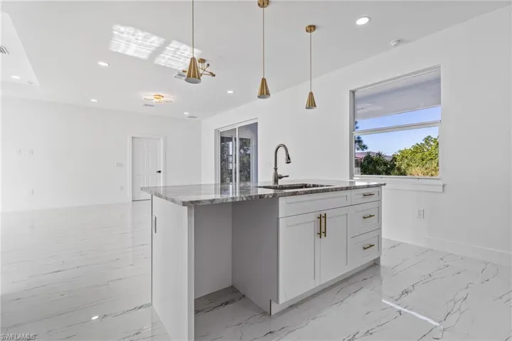 Kitchen featuring light stone counters, white cabinetry, a kitchen island with sink, pendant lighting, and light marble finish flooring