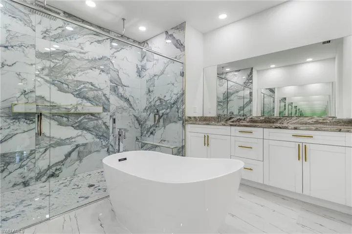 Bathroom with a freestanding bath, a marble finish shower, vanity, recessed lighting, and stone wall
