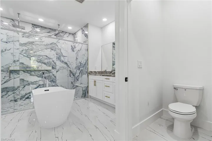 Bathroom with a marble finish shower, a freestanding bath, vanity, recessed lighting, and light marble finish floors