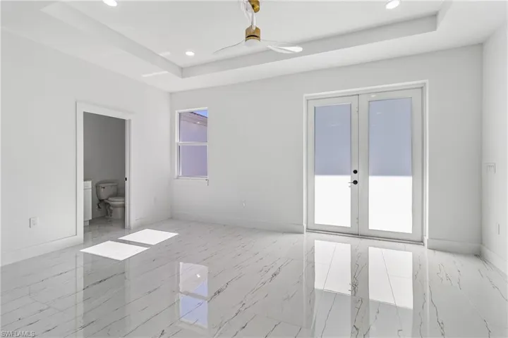 Unfurnished bedroom featuring french doors, a tray ceiling, ceiling fan, recessed lighting, and connected bathroom