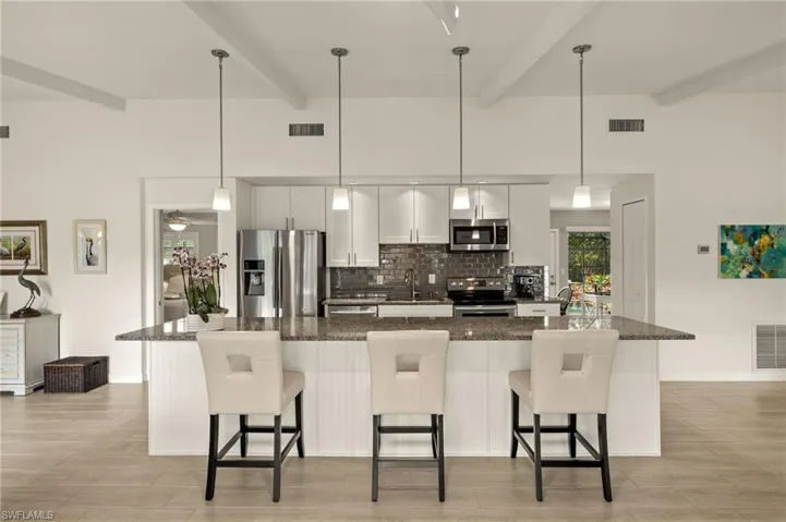 Kitchen featuring stainless steel appliances, decorative backsplash, white cabinets, a large island with sink, and a kitchen bar